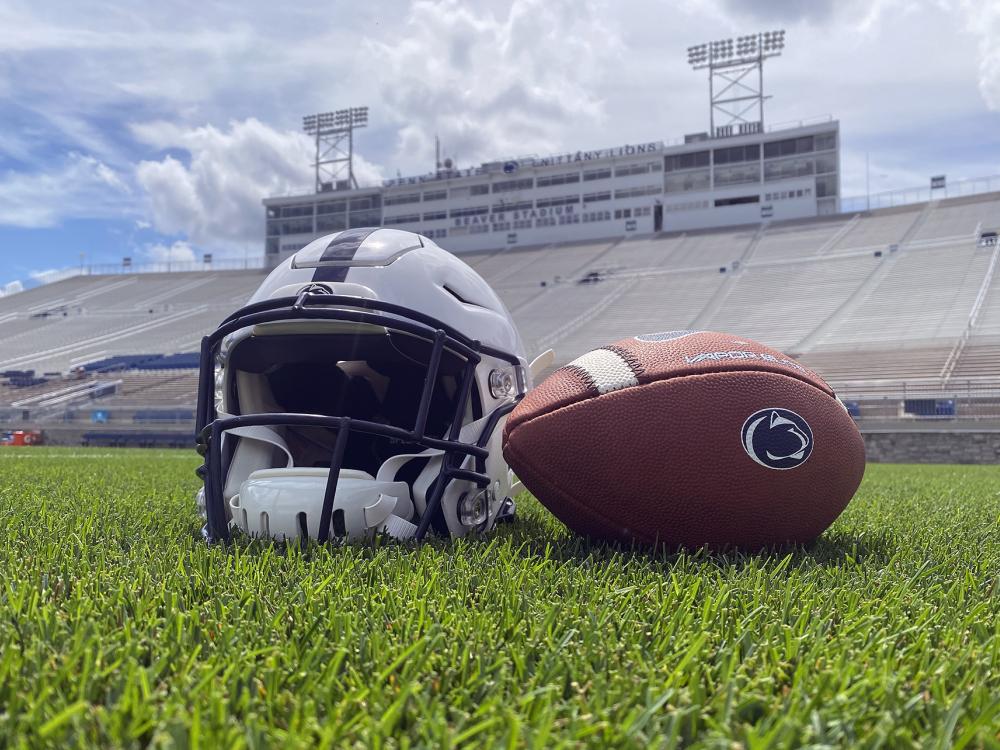 A football and helmet on the field at Beaver Stadium